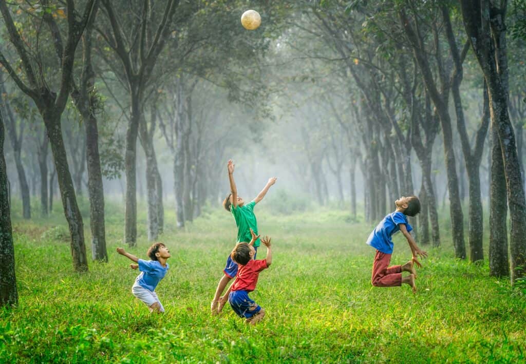 Four children jumping to reach a soccer ball in a field.