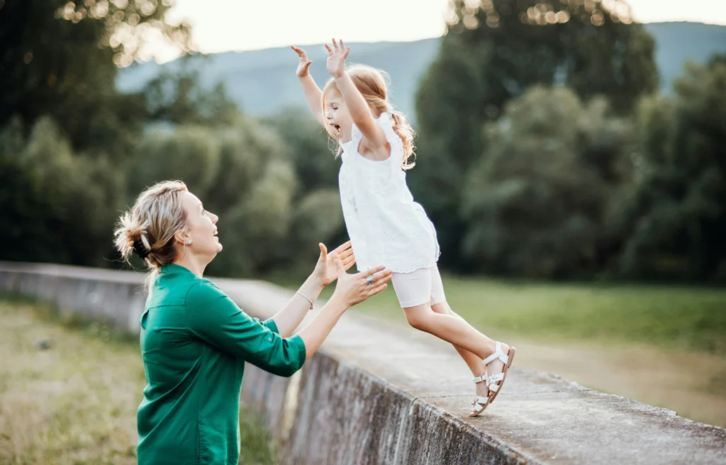 woman catching a young girl as she jumps off a block