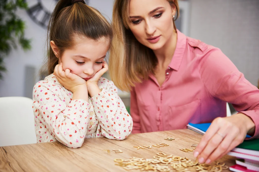 a woman and a girl spelling words on a table with letter tiles